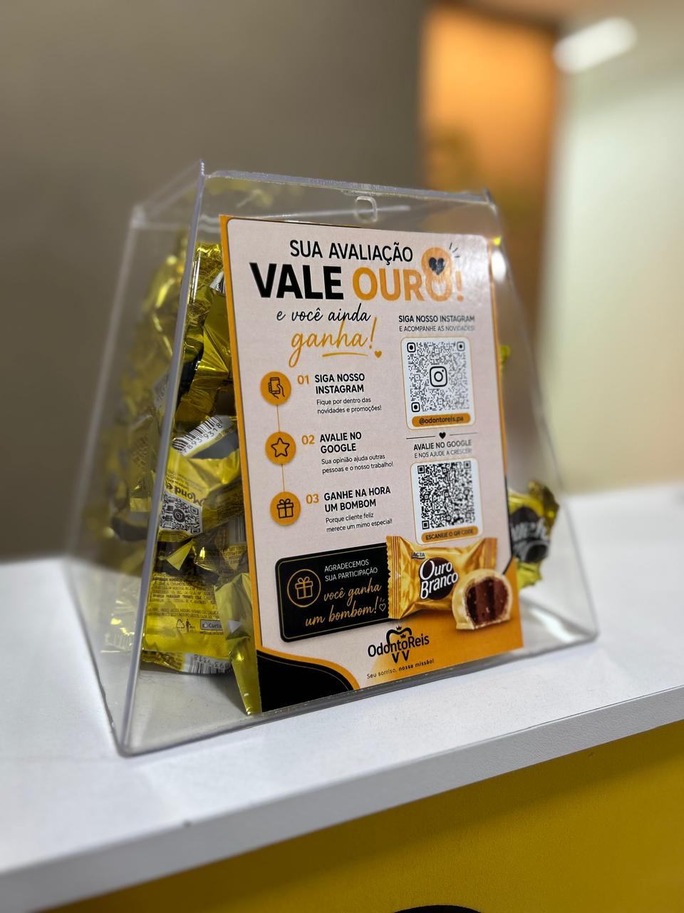 Display na recepção convidando pacientes a avaliar a clínica e ganhar um bombom